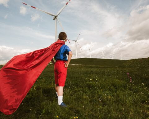 Will optimism solve climate change? | Image of a person on a wind farm wearing a red cape